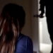Unrecognizable blonde girl sitting back to camera, the door opens and a man enters the room and stands facing her, waist down.