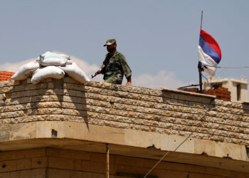 In this Tuesday, July 17, 2018, photo, a Russian flag waves as a Syrian soldier walks on a roof of a military post overlooking the Damascus-Aleppo highway in the town of Rastan, Syria. Rastan and nearby Talbiseh were among the first Syrian towns to carry weapons against the government when the uprising against President Bashar Assad began in 2011. As the Syrian government reasserts control over opposition strongholds, co-existence between the military and former rebel fighters who surrendered is the new reality. (AP Photo/Hassan Ammar)
